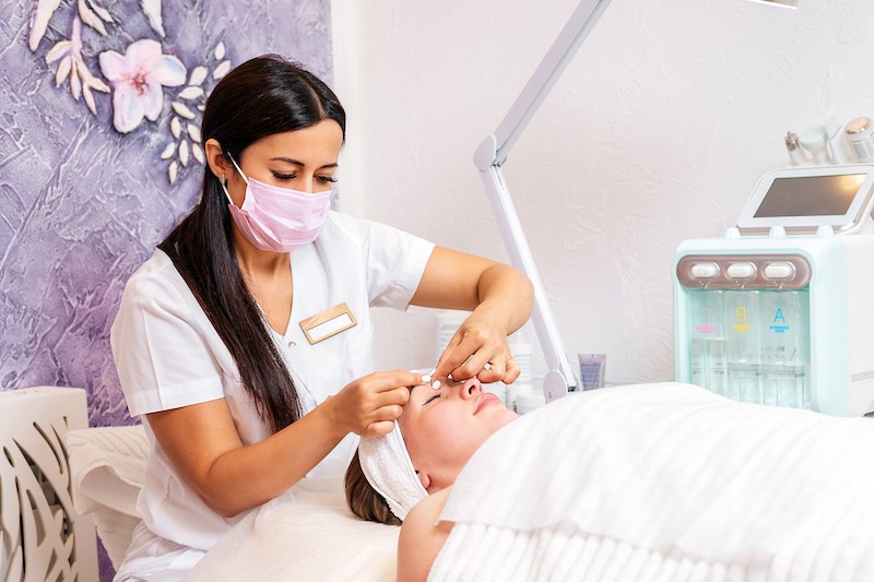 A Cosmetologist in A face mask Does A Facial Massage
